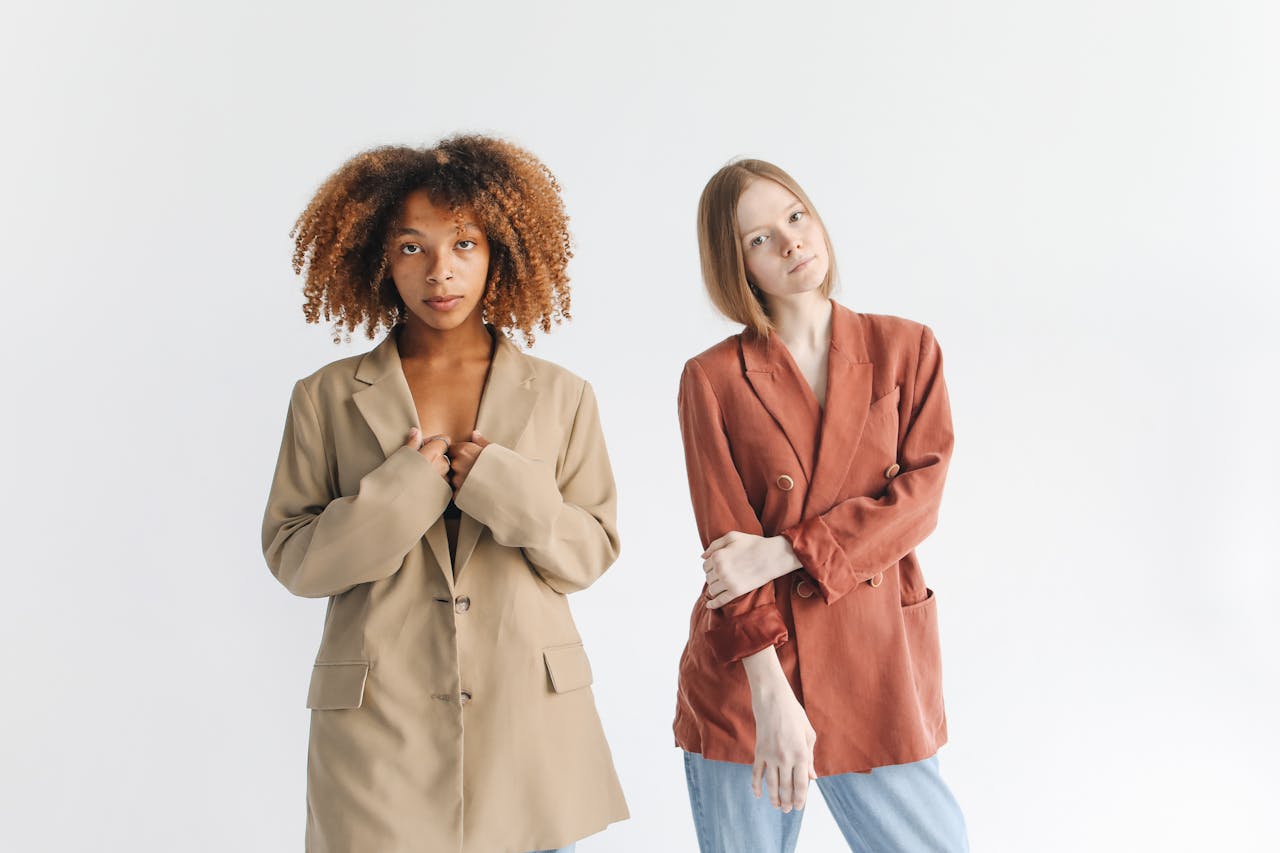 Two women modeling fashionable blazers in a studio setting with a white backdrop.