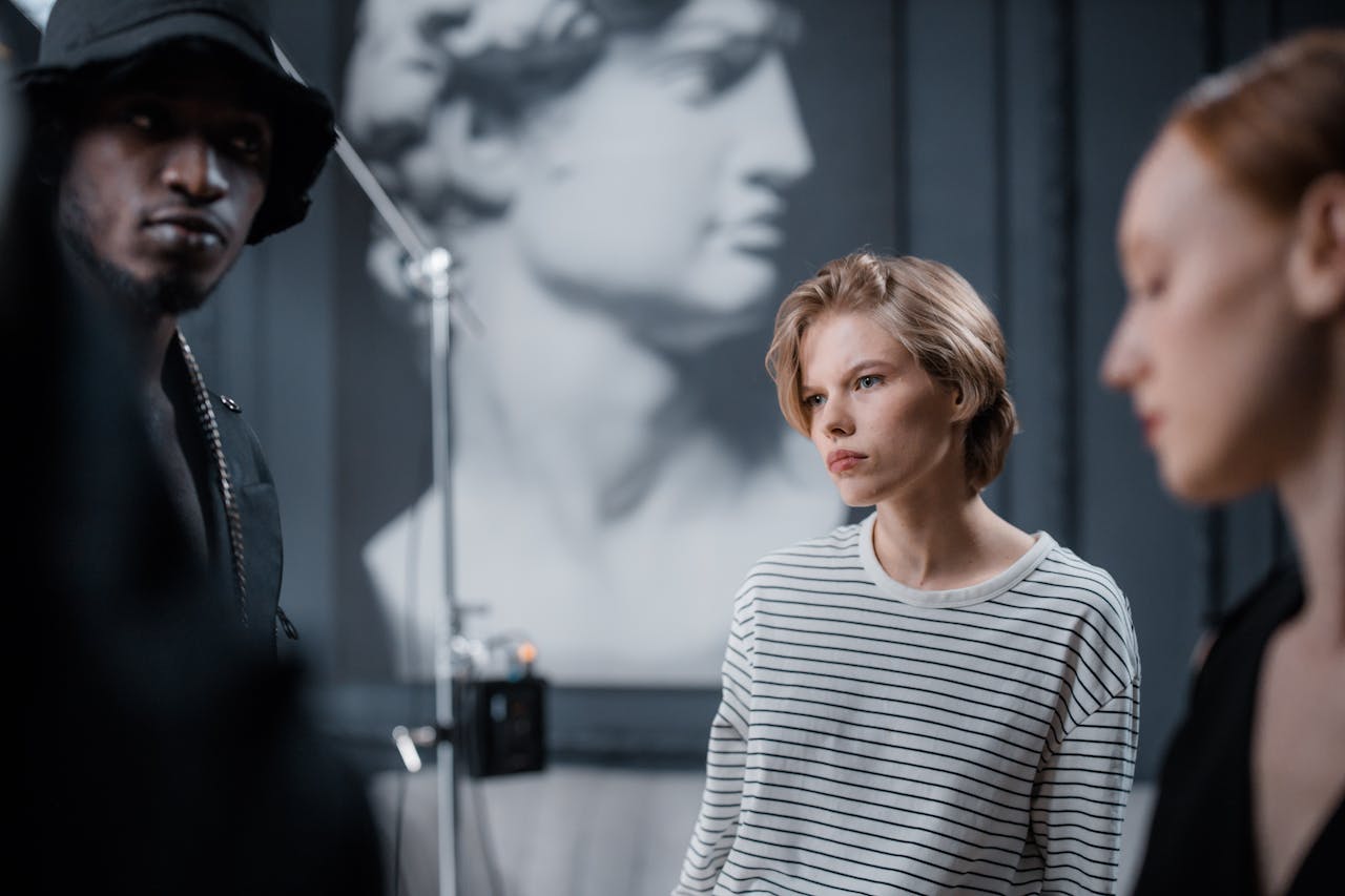 Three models in a fashion photoshoot with blurred classical sculpture background in a studio.